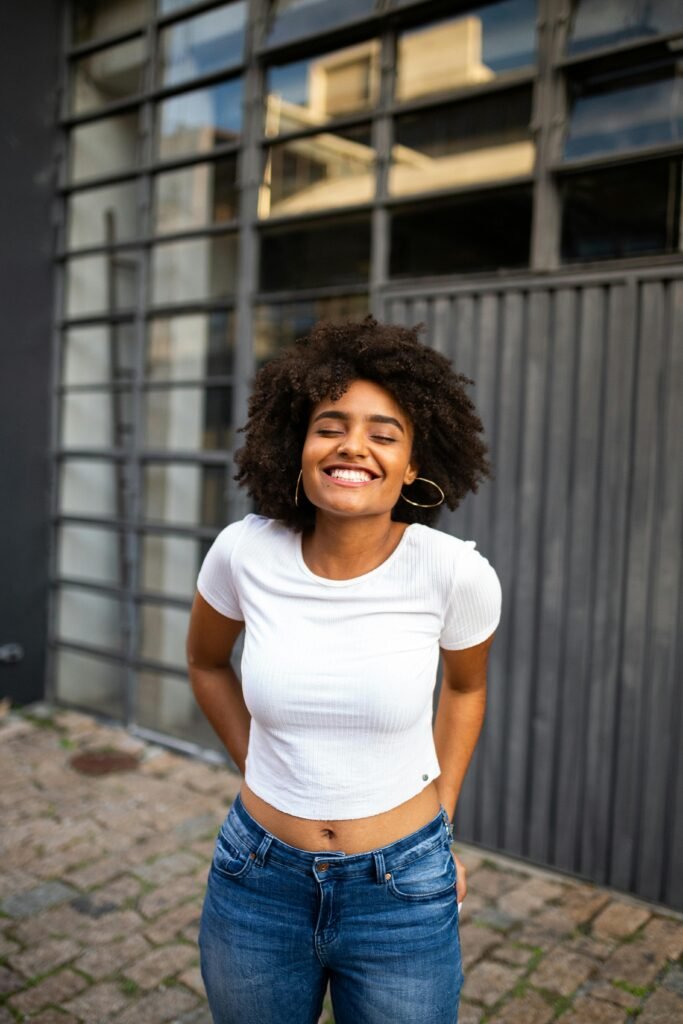 Smiling woman with curly hair in casual fashion enjoys a bright day outdoors.
