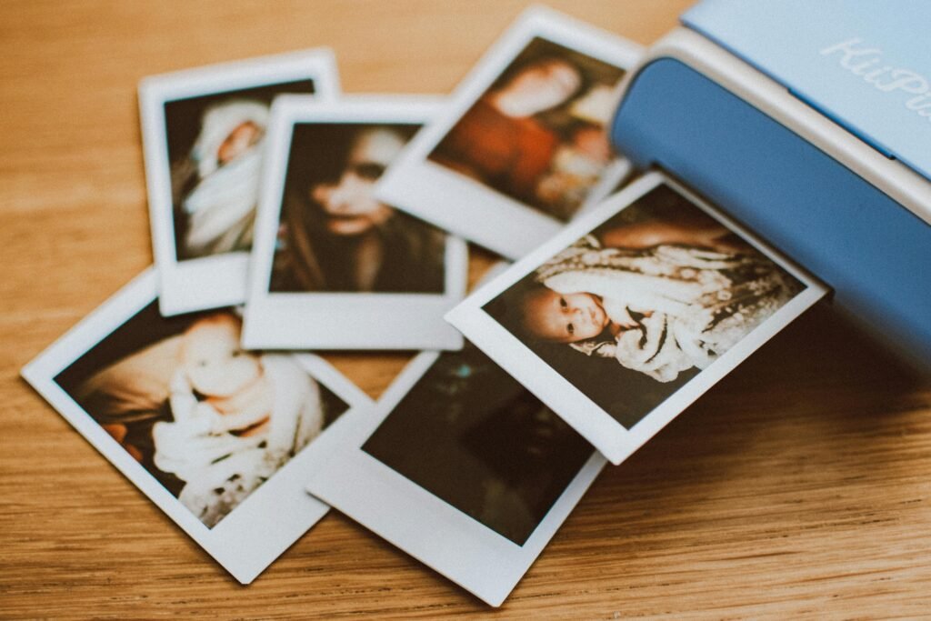 A collection of instant photo prints scattered on a wooden table, featuring personal moments.