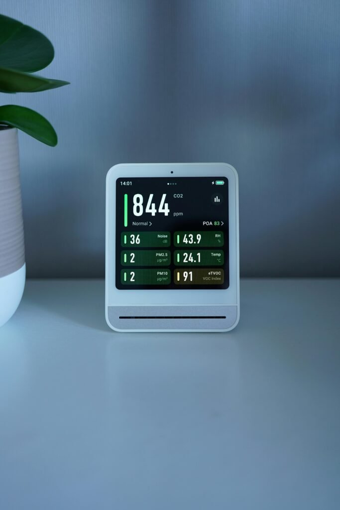 A sleek air quality monitor displays CO2 and particle levels, set on a modern desk indoors.