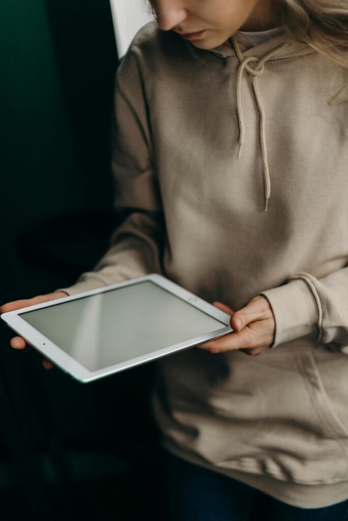 A woman in a hoodie holding a tablet indoors, reflecting a modern home lifestyle.