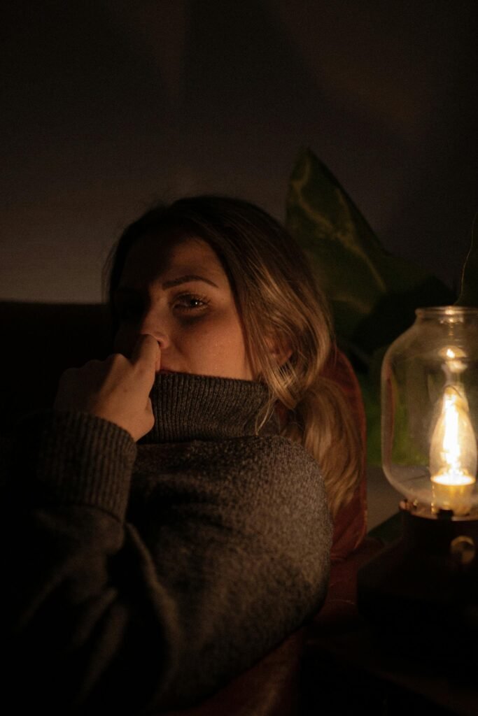 A woman in a dark cozy setting, illuminated by a dim lamp, evokes a warm, introspective mood.